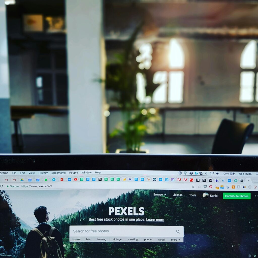 A close-up of a laptop displaying the Pexels website in a sunlit, modern office.